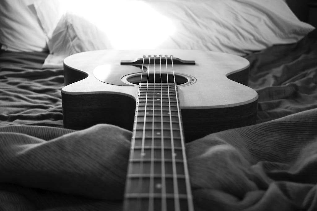 Monochrome image of an acoustic guitar resting on a bed, capturing musical essence.