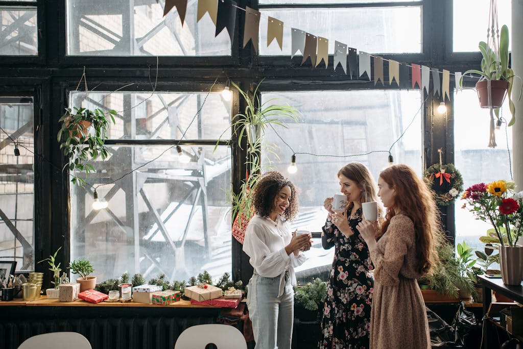 A joyful indoor gathering of friends drinking coffee, surrounded by festive decorations and plants.