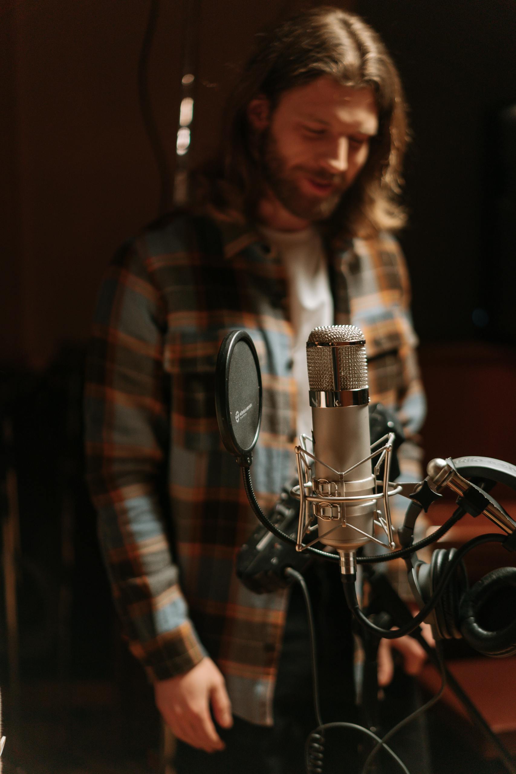 Male musician in recording studio with condenser microphone, captured in a warm, moody atmosphere and signifying a person who engages in therapy with Musician Therapy Collective.