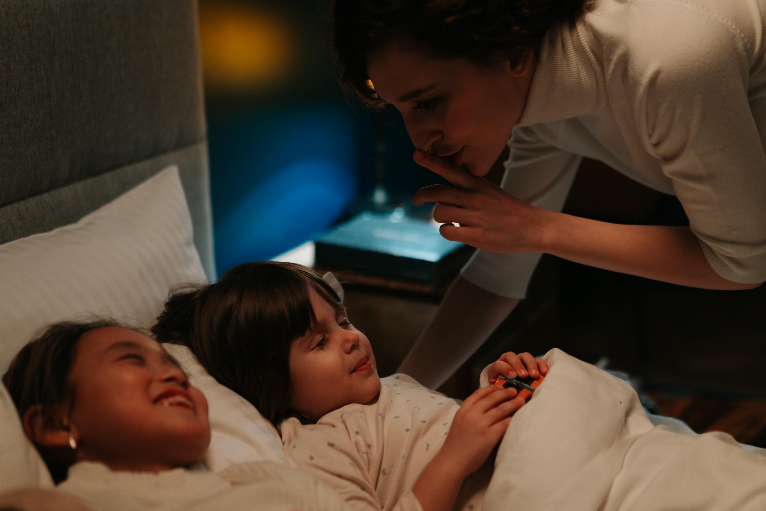 A caring woman comforting children at bedtime with a soothing gesture.