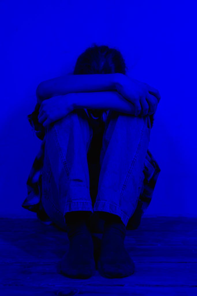 A person sits alone in a dark blue light, conveying feelings of sadness and solitude.