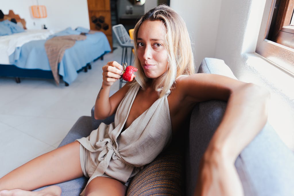 A relaxed woman enjoying a fresh strawberry while lounging in a modern indoor setting.