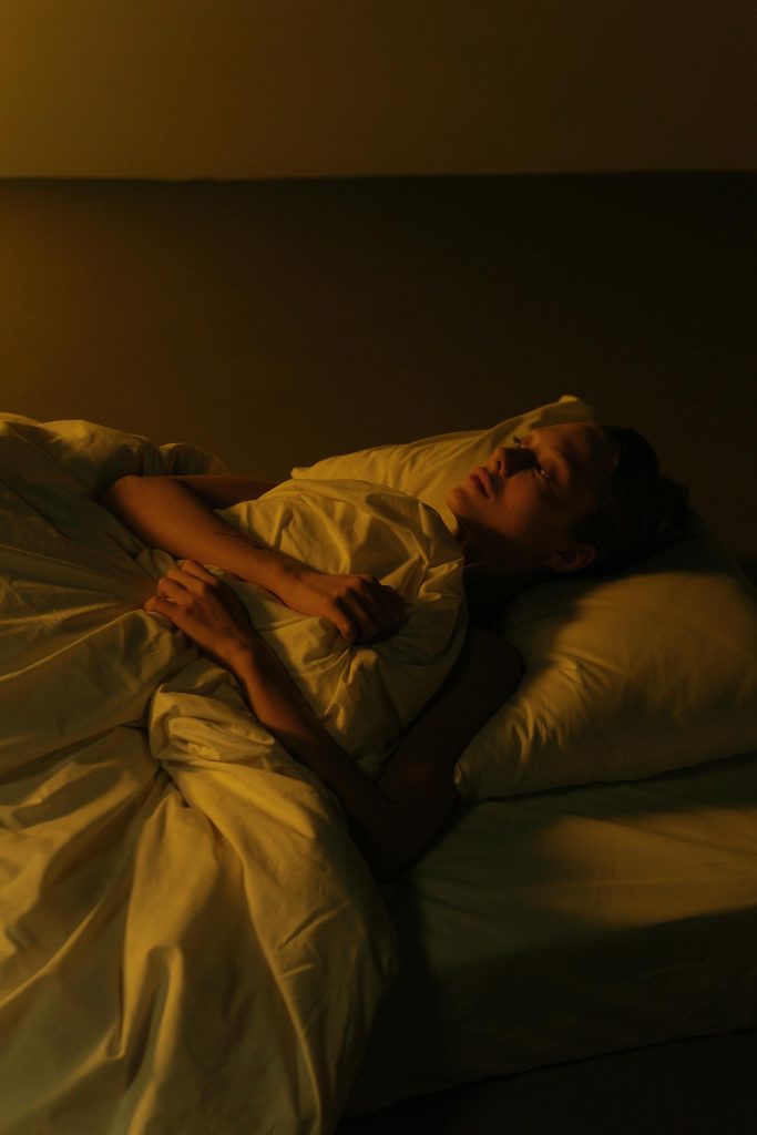 A serene woman rests in bed amidst warm, subdued lighting at night, creating a relaxing atmosphere.