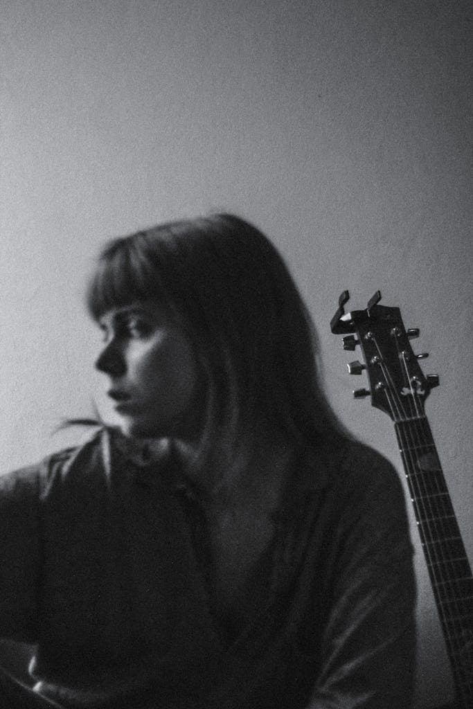 A thoughtful black and white portrait of a young woman sitting with a guitar, conveying a serene and contemplative mood.