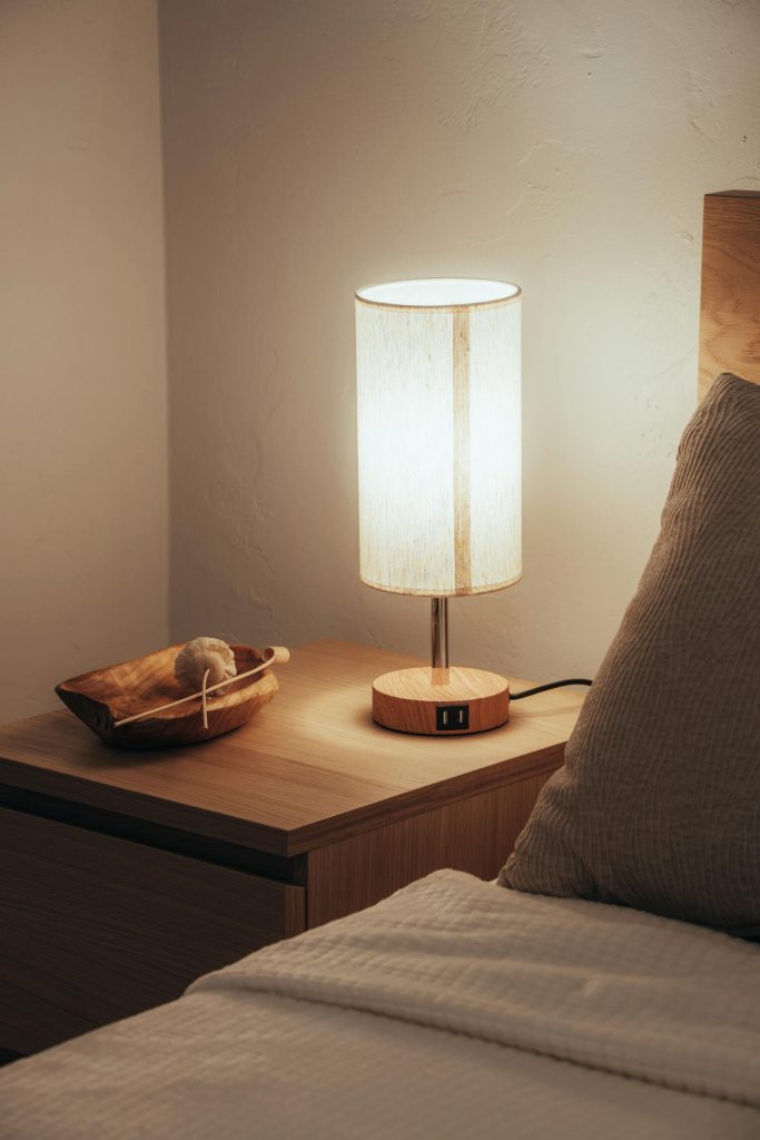 A warm and inviting bedroom scene with a glowing lamp on a wooden nightstand.