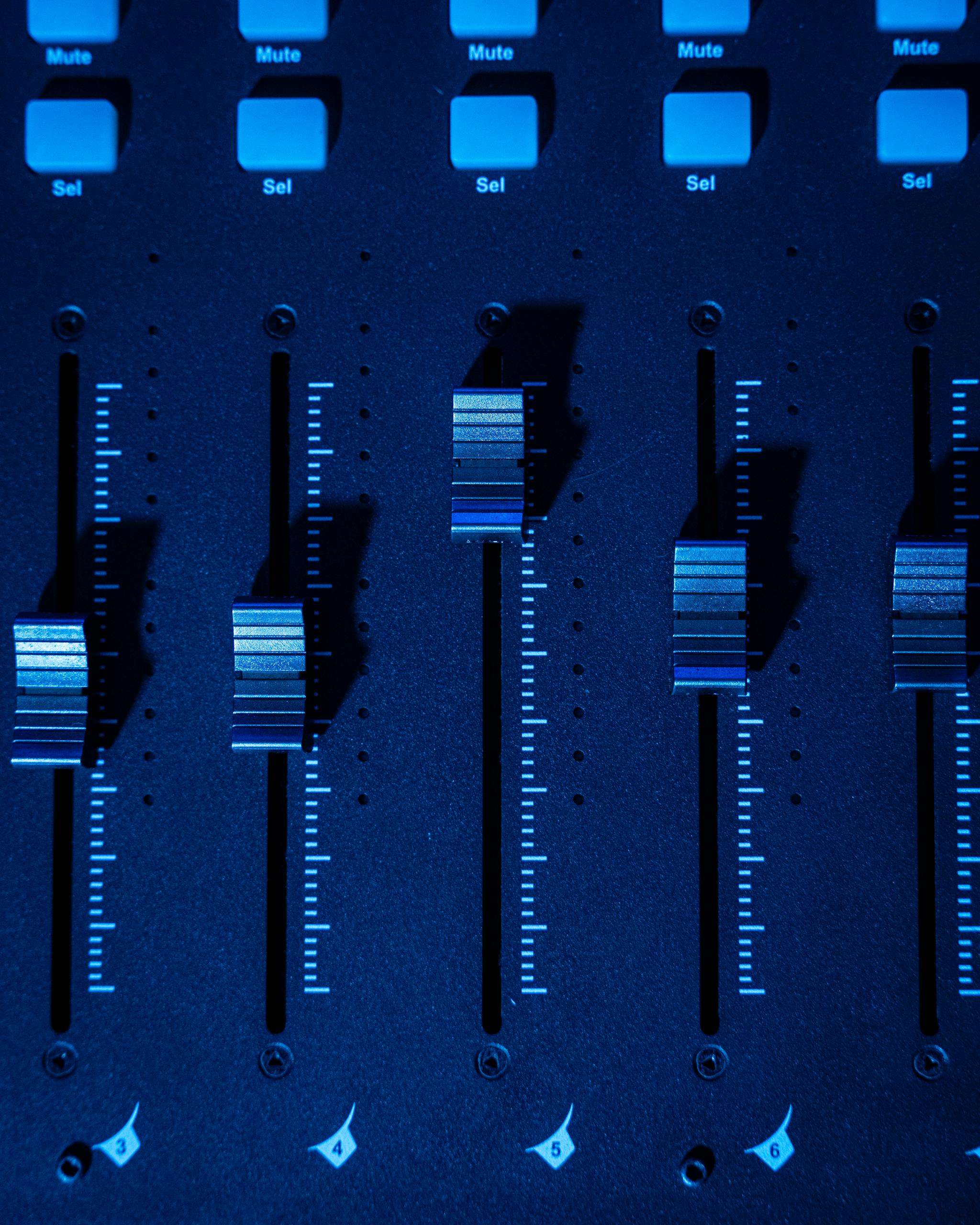 Detailed shot of a mixing console faders with blue lighting, ideal for music production themes.