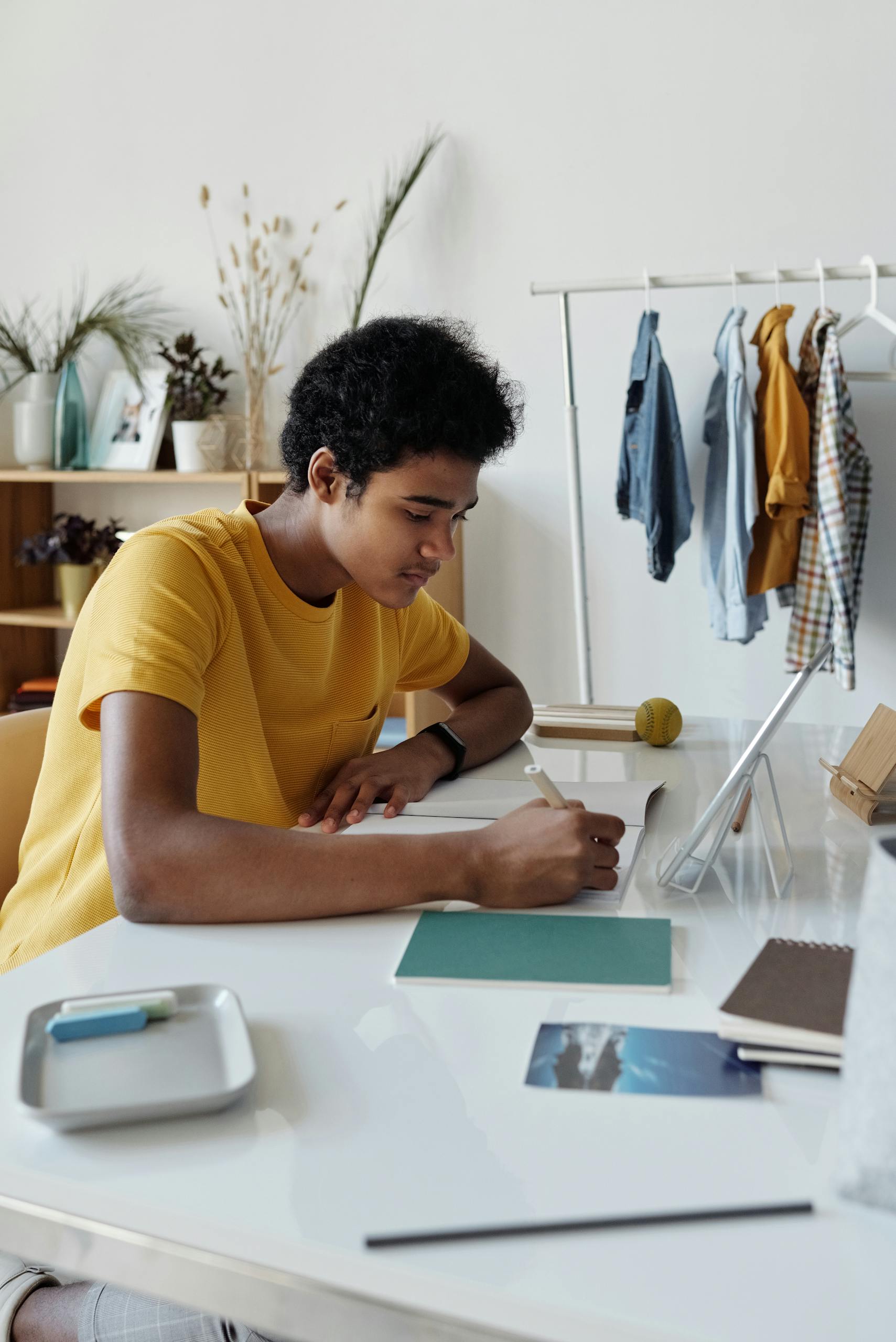 Focused African American teen studying indoors with a tablet and notebook at home.