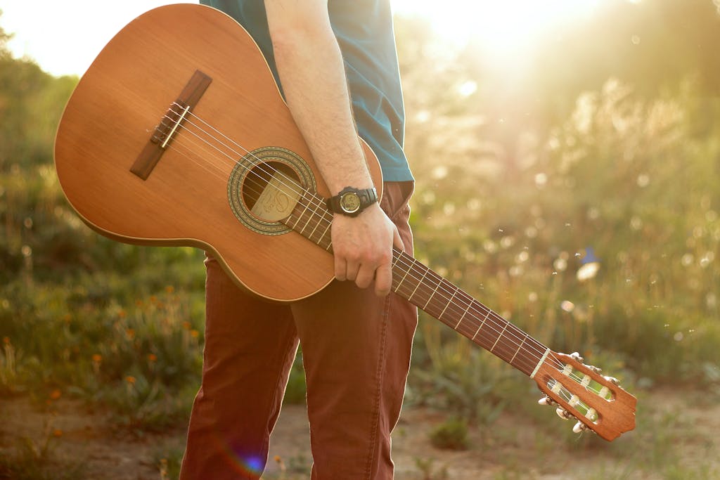 Man holding an acoustic guitar in a sunlit meadow during summer, showcasing nature and music.