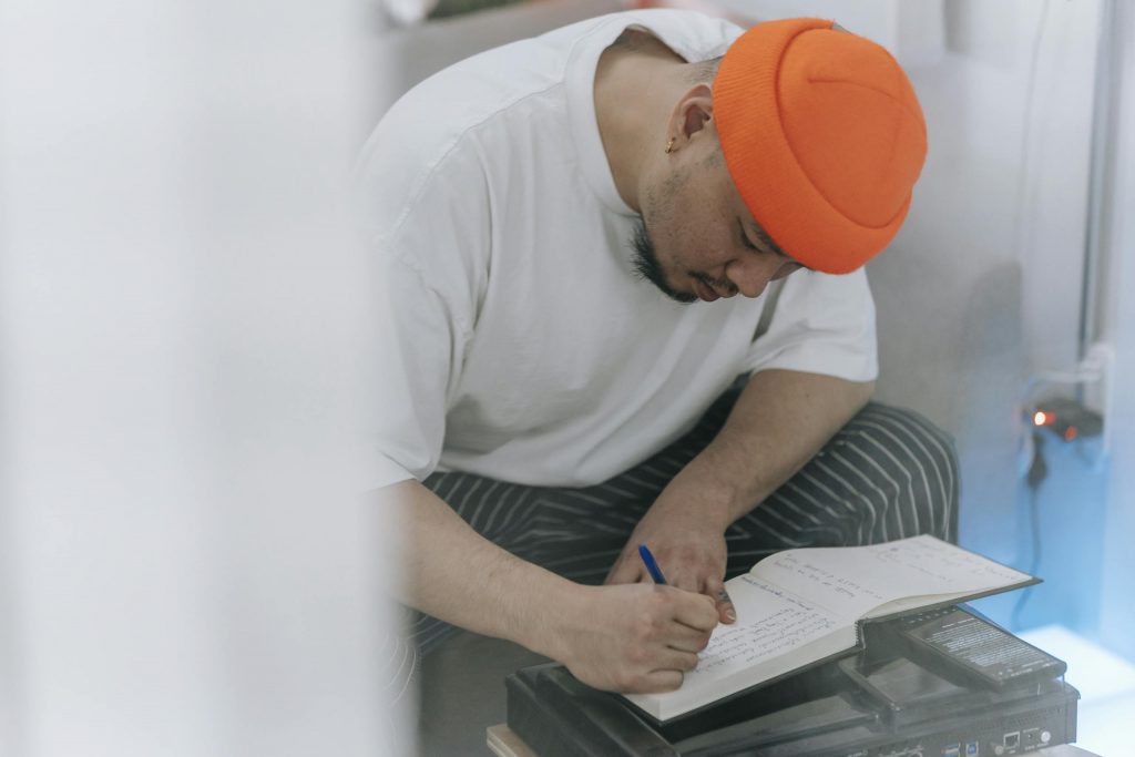 Man in an orange beanie writing in a notebook, showcasing creativity and focus.