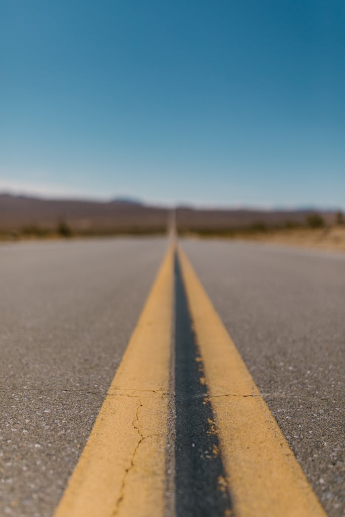 Straight desert highway with yellow lines stretching into the horizon under a vibrant blue sky.