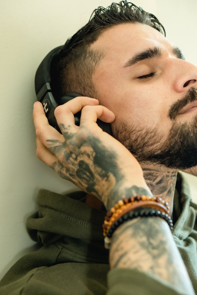 Close-up of a bearded man enjoying music with headphones, eyes closed, tattoos visible.