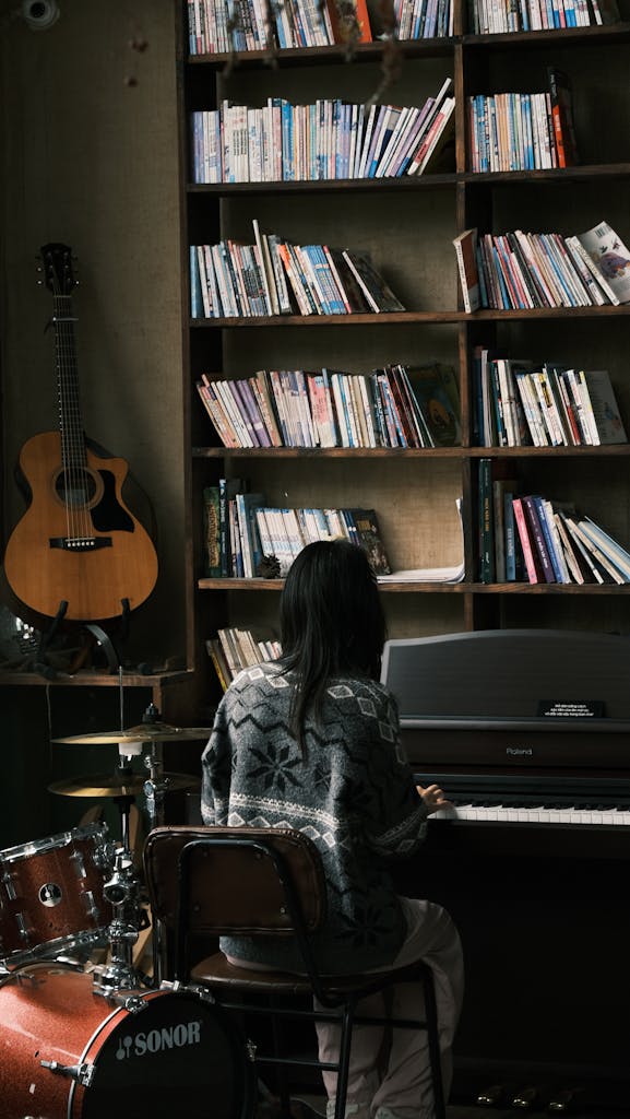 Woman playing piano in a library with guitar and drums nearby, evoking a creative atmosphere.